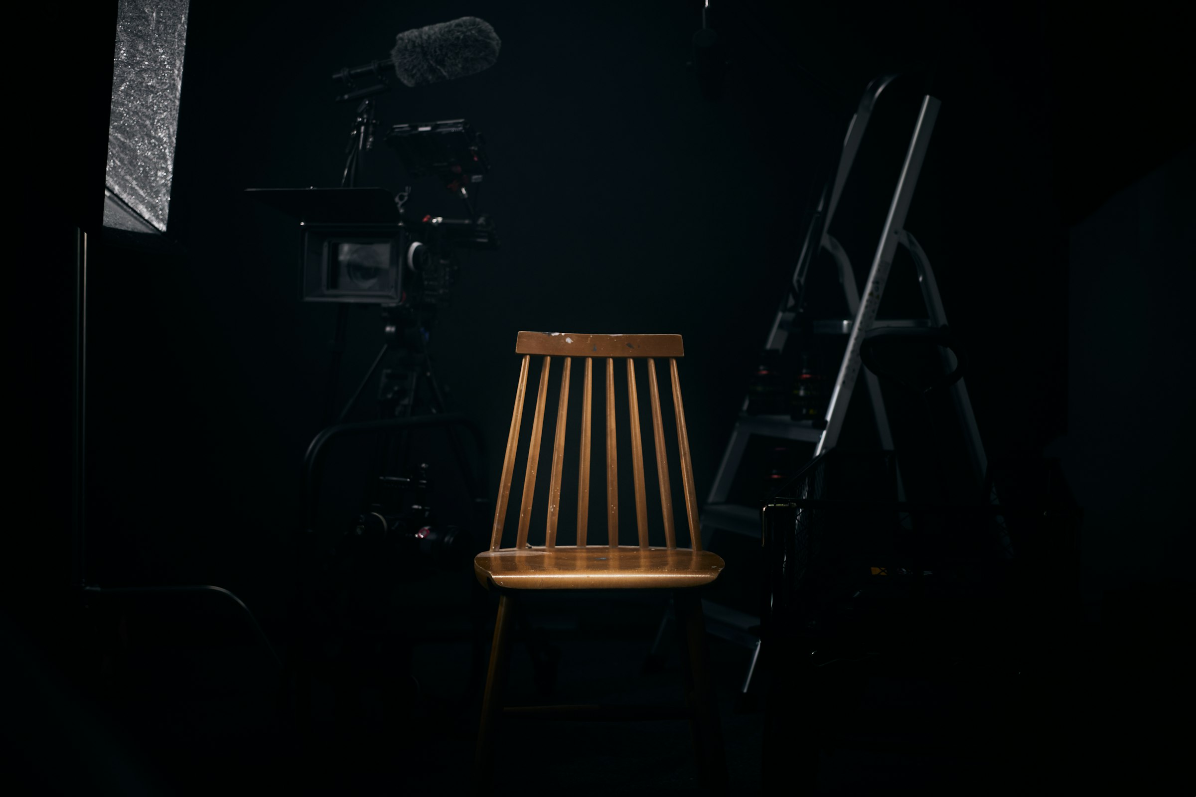 A dark cinematic studio with a chair, boom microphone and lighting rig